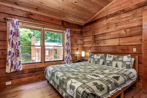 A wooden cabin bedroom with a bed, two windows, a nightstand, and a lamp. - Charming Romantic Cabin Escape with Private Hot Tub in Sevierville, Tennessee (Sevierville)