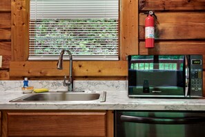 A kitchen with a sink, a microwave, and a fire extinguisher mounted on the wall. - Charming Romantic Cabin Escape with Private Hot Tub in Sevierville, Tennessee (Sevierville)
