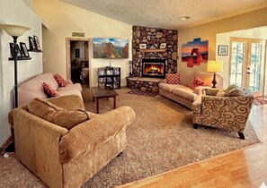 Una sala de estar con chimenea, sofás, una mesa de centro y una estantería.