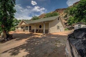 Ein zweistöckiges Haus mit verdeckter Veranda, einem Steinfundament und einem großen Felsen davor.
