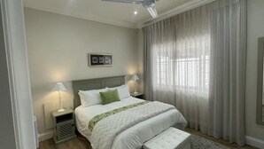 A bedroom with a bed, bedside lamps, a ceiling fan, and a window with curtains. - Discover Cape Town from Your Stylish Upper Claremont Garden Cottage (Cape Town)
