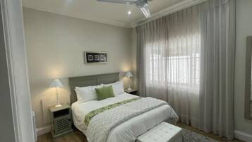 A bedroom with a bed, bedside lamps, a ceiling fan, and a window with curtains.