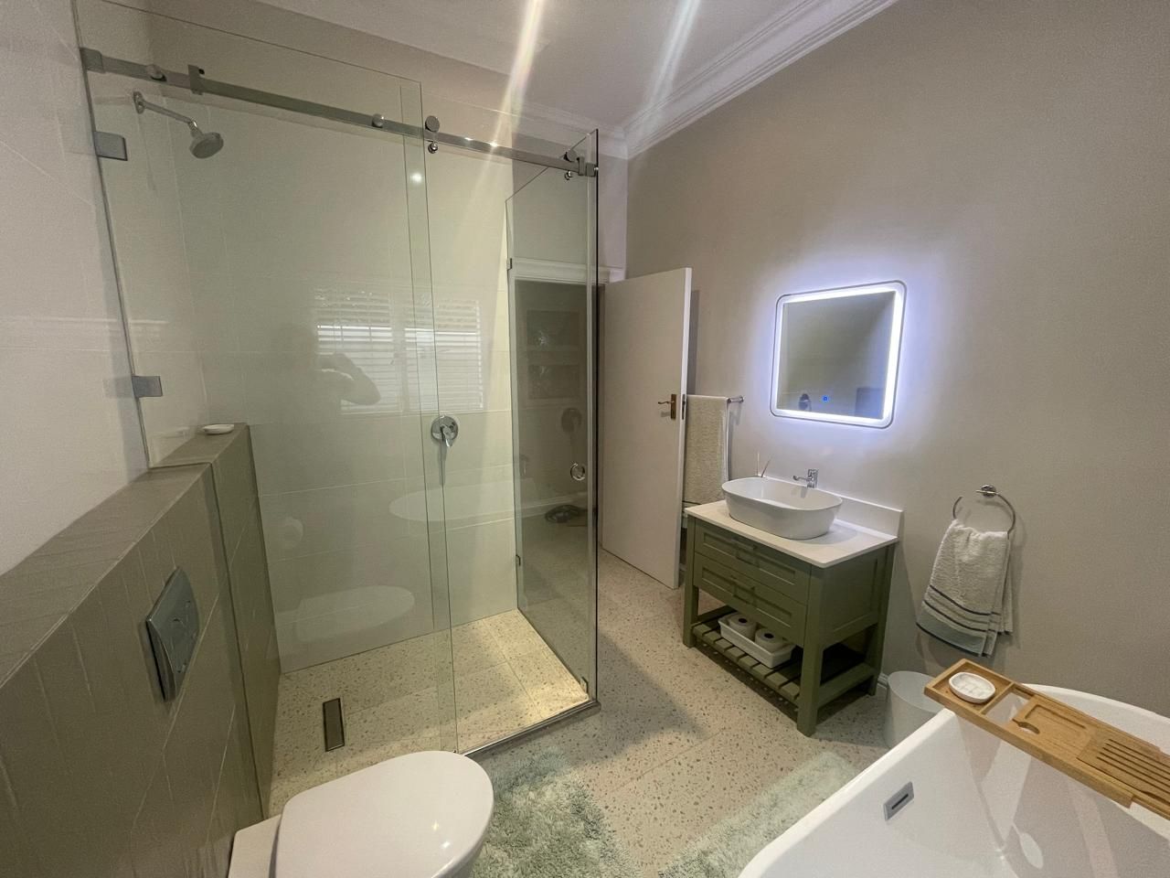 A modern bathroom with a glass shower enclosure, a white sink, and a wooden vanity.