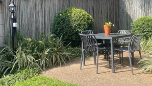 A patio with a table and chairs, surrounded by a wooden fence and greenery. - Discover Cape Town from Your Stylish Upper Claremont Garden Cottage (Cape Town)