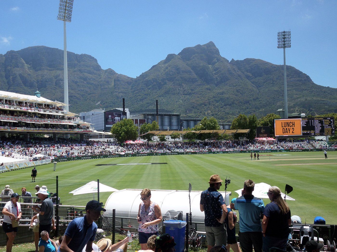 A stadium with a large crowd, a scoreboard, and mountains in the background.