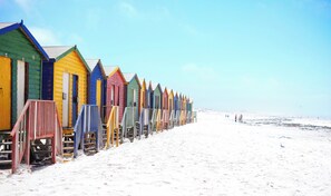 En rad färgglada strandhytter med trappsteg som leder upp till dem, belägna på en sandstrand.