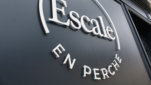 En skylt med ordet ”Escale” och frasen ”EN PERCHÉ” mot en mörk bakgrund.