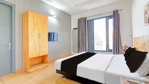 Una habitación de hotel con cama, armario, ventilador de techo, ventana con cortinas y televisor montado en la pared.