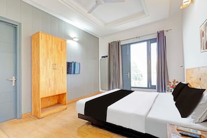 Una habitación de hotel con cama, armario, ventilador de techo, ventana con cortinas y televisor montado en la pared.