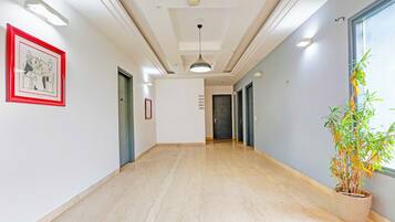 A hallway with a marble floor, a framed picture on the left, and a potted plant on the right.