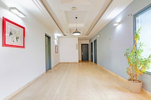 A hallway with a marble floor, a framed picture on the left, and a potted plant on the right. - Townhouse Oak Omaxe City Centre Gurgaon (Gurugram)