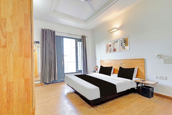 A hotel room with a large bed, a wooden headboard, a bedside table with a lamp, and a window with curtains. - Townhouse Oak Omaxe City Centre Gurgaon (Gurugram)