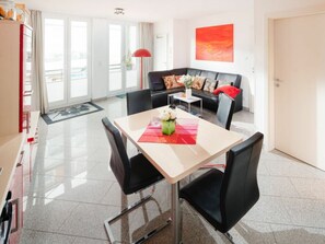 A modern hotel room with a dining area, a sofa, and a large window. - Holiday Apartment With 1 Bedroom (Norderney)