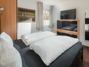 A hotel room with a bed, a TV, a window with curtains, and a wooden cabinet. - Holiday Apartment With 1 Bedroom (Norderney)