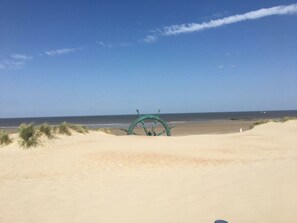 Ein Strand mit einer großen grünen Struktur, vermutlich einem Rettungsturm, und einem klaren Himmel.