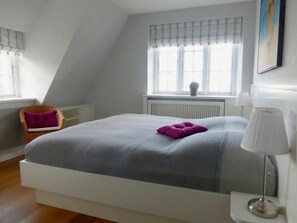 A bedroom with a bed, a chair, a window with curtains, a radiator, and a lamp. - 1 in the Muhlenblick House (Borgsum)