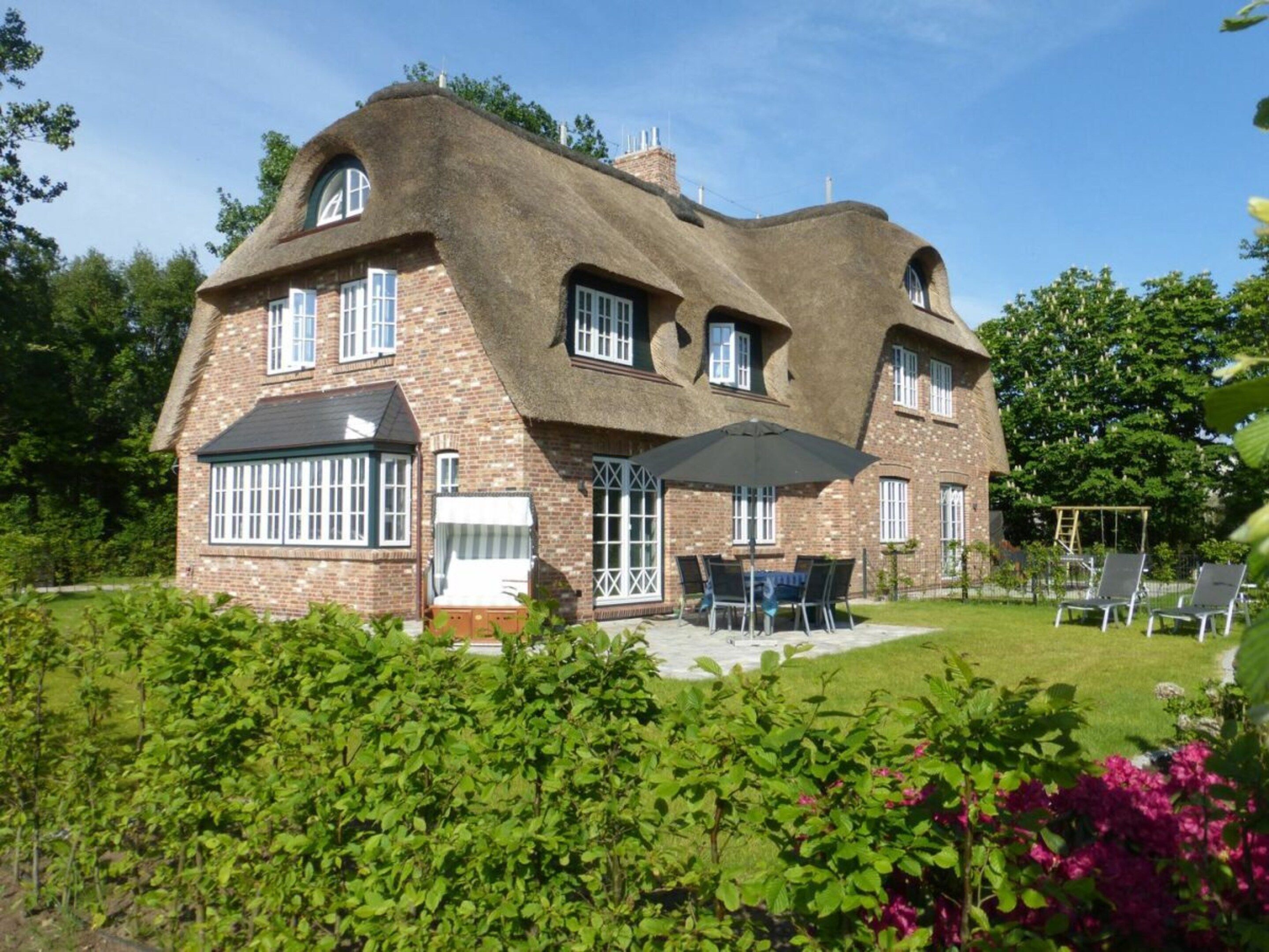A large brick house with a thatched roof, multiple windows, and a patio area with outdoor furniture.