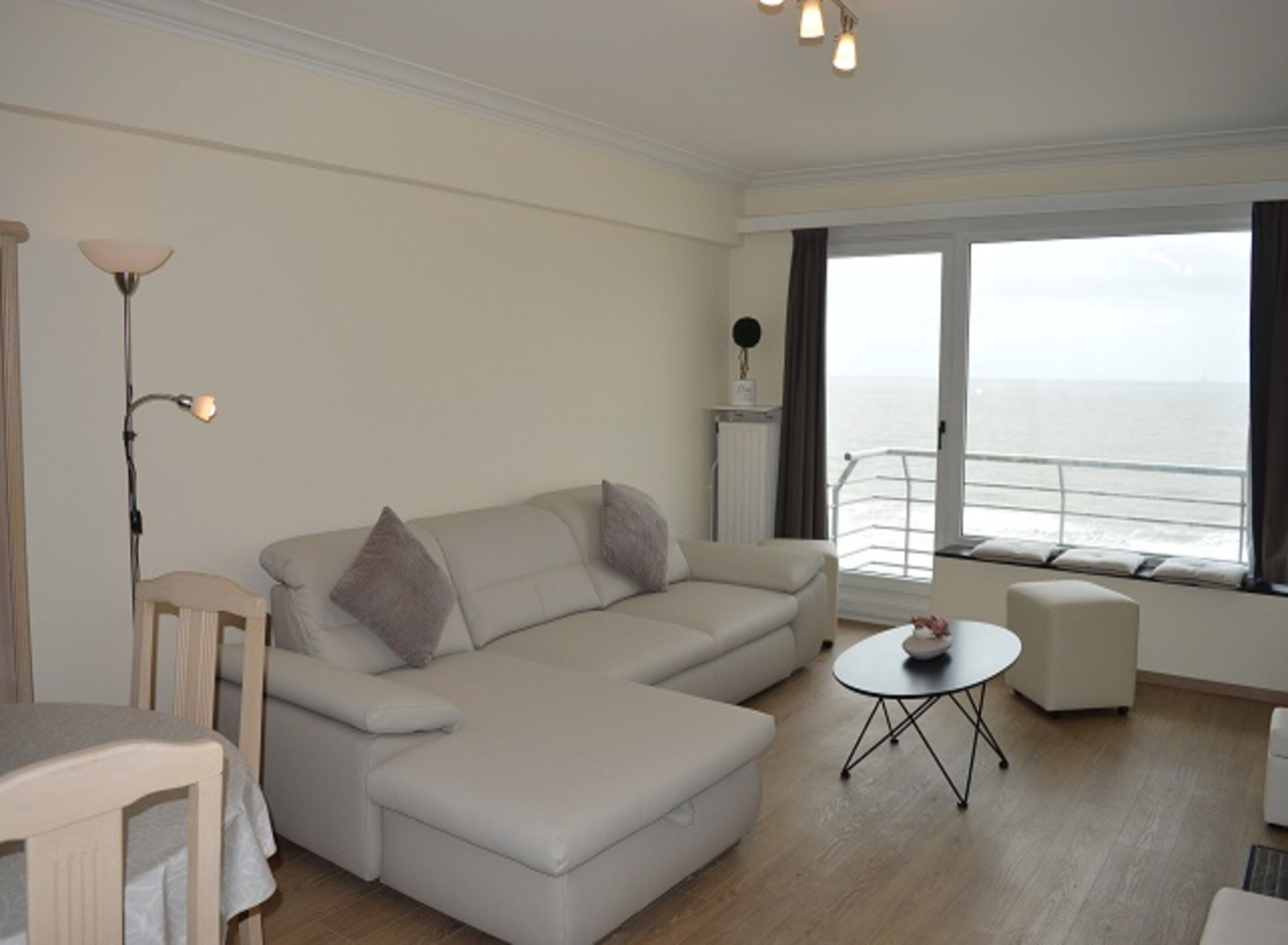 A modern living room with a sofa, a small table, and a view of the sea through large windows.