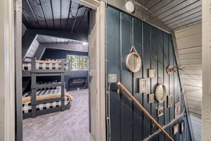 A room with bunk beds, a dark wooden door with a handrail, and various framed items on the wall. - Modern A-Frame Cabin with Hot Tub Near Yellowstone, Island Park, Idaho (Island Park)