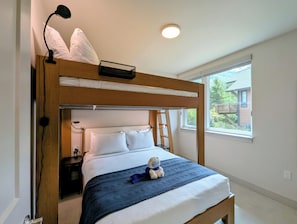 A bunk bed with a headboard, a bedside table, a lamp, and a window with a view of greenery. - NEW BUILD! King Bed | Shuttle to Slopes (Keystone)