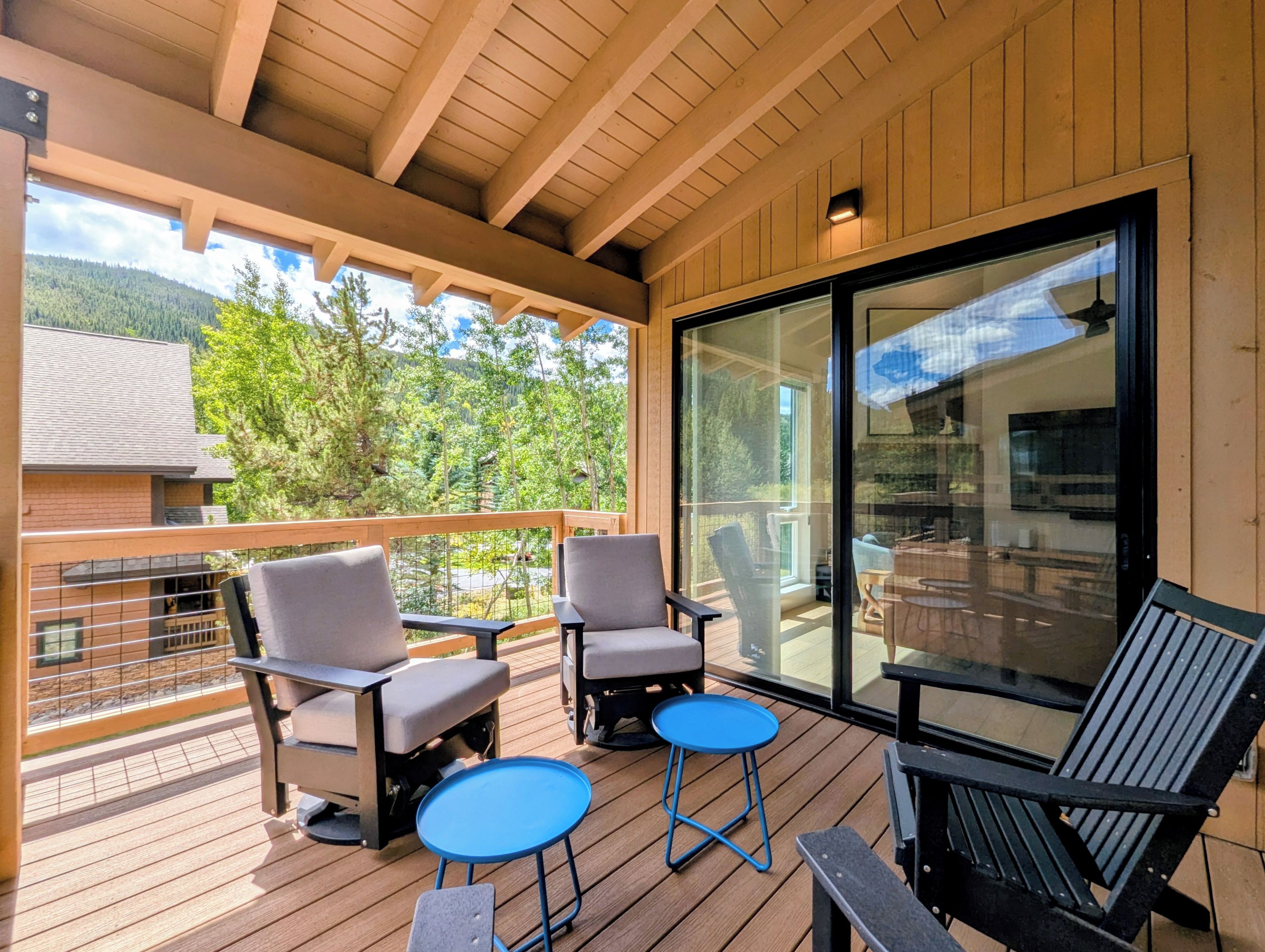 Una terraza de madera con mobiliario exterior, incluyendo sillas y una pequeña mesa, con vistas a un paisaje montañoso.
