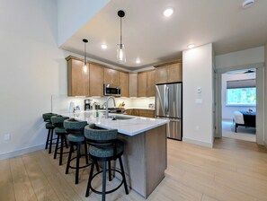 A modern kitchen with a central island, bar stools, stainless steel appliances, and pendant lighting. - NEW BUILD! King Bed | Shuttle to Slopes (Keystone)