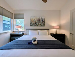 A hotel room with a large bed, two bedside tables, a window with blinds, a painting on the wall, and a stuffed toy on the bed. - NEW BUILD! King Bed | Shuttle to Slopes (Keystone)