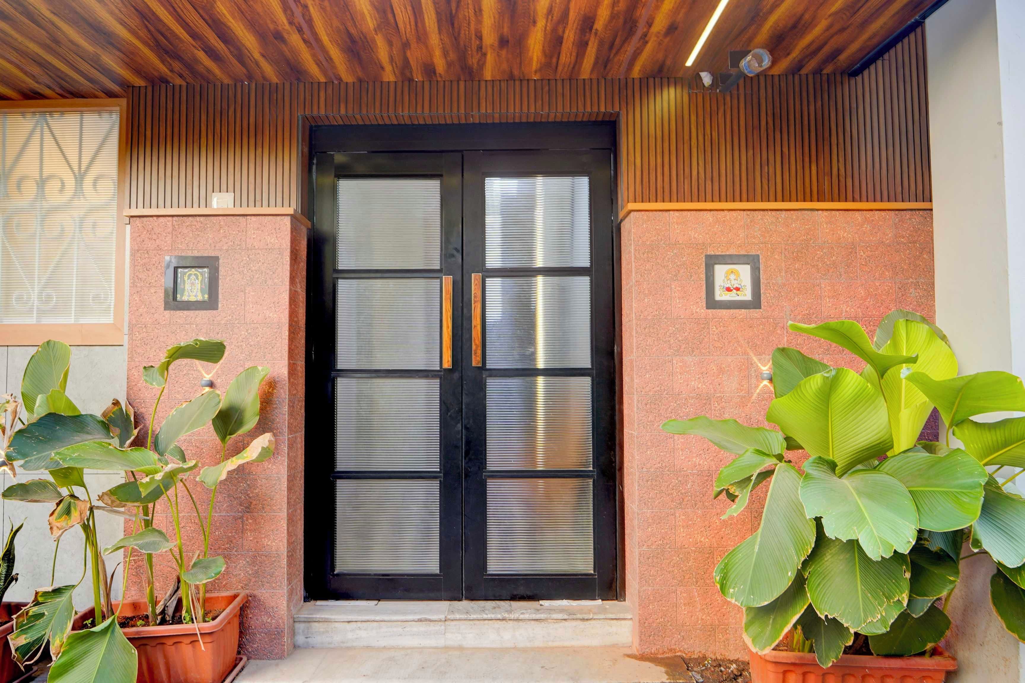 Entrada de hotel com porta preta, plantas em vasos e teto de madeira.