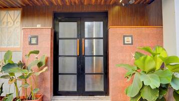 Entrada de hotel com porta preta, plantas em vasos e teto de madeira.
