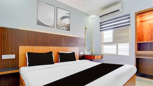 Un dormitorio moderno con cabecera de madera, una cama grande con ropa de cama blanco y negro, dos obras de arte en la pared, un equipo de aire acondicionado y una ventana con persianas.