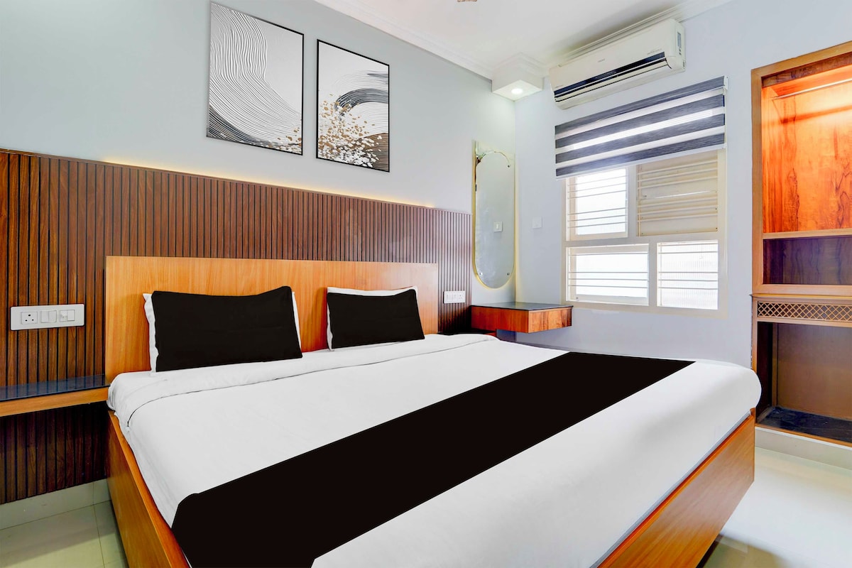 Een moderne slaapkamer met een houten hoofdeinde, een groot bed met zwart-wit beddengoed, twee kunstwerken aan de muur, een airconditioning en een raam met zonwering.