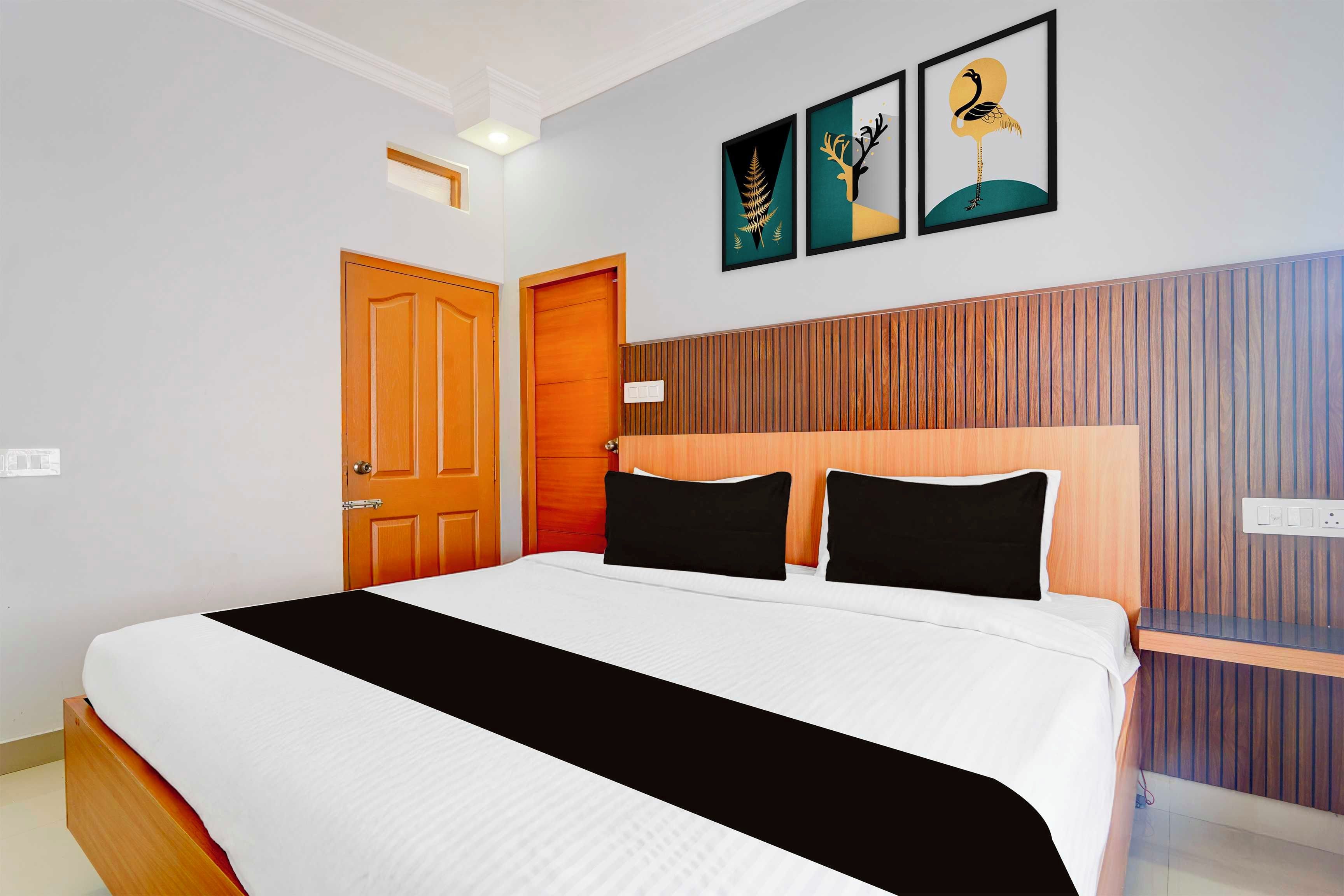 A hotel room with a bed, wooden headboard, two black pillows, a white bedspread, and three framed wall art pieces.