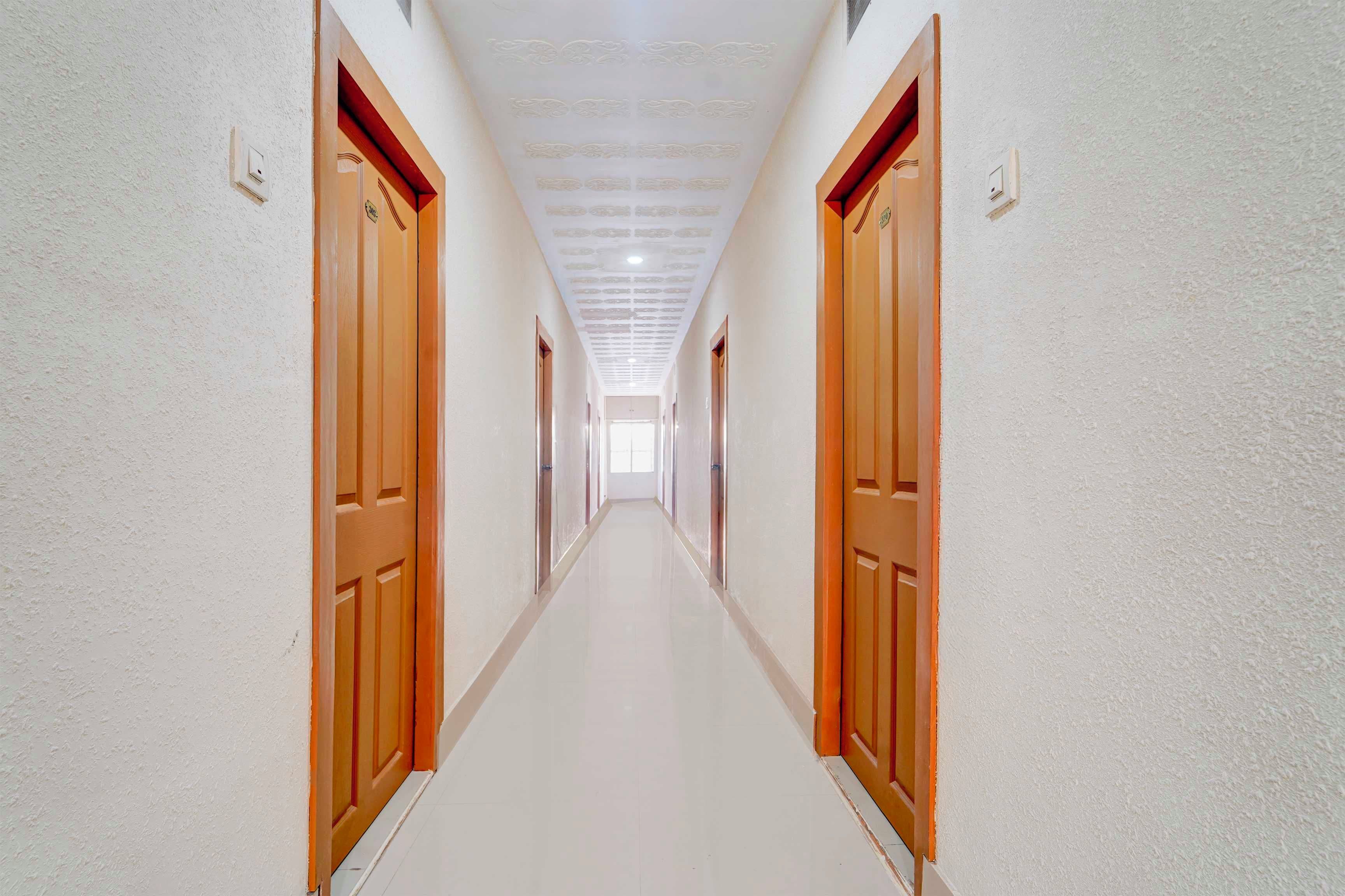 Um corredor comprido e estreito com portas de madeira em ambos os lados, que leva a um quarto claro no final.
