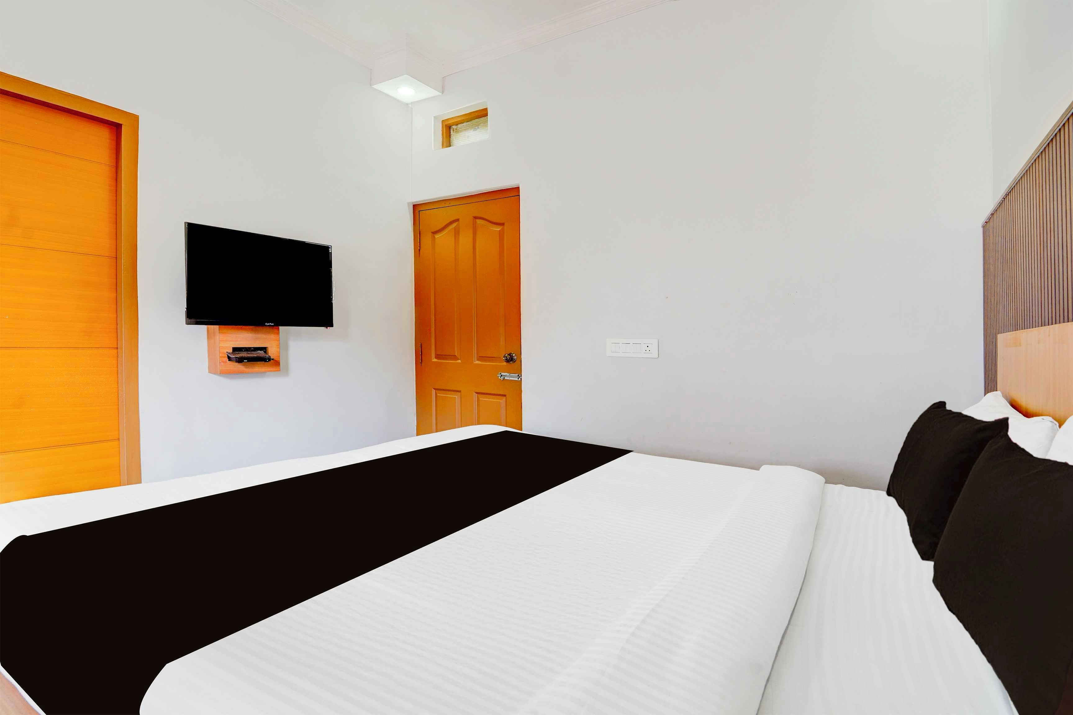 A hotel room with a bed, a television mounted on the wall, and a wooden door.