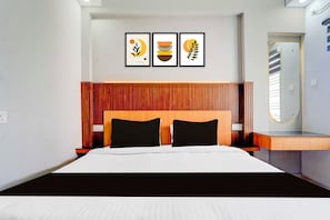 Une chambre d’hôtel avec un lit, une tête de lit en bois, une table de chevet, un miroir et trois œuvres d’art encadrées accrochées au mur.