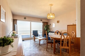 A hotel room with a balcony, a dining table with chairs, a sofa, a chandelier, and a potted plant. - Apartment in Blankenberge Near Belgian Pier (Blankenberge)