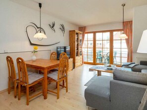 A modern living room with a wooden dining table, chairs, a sofa, and a TV. - 1.5/t3 Holiday Home Park \"freesenbruch\" (Zingst)
