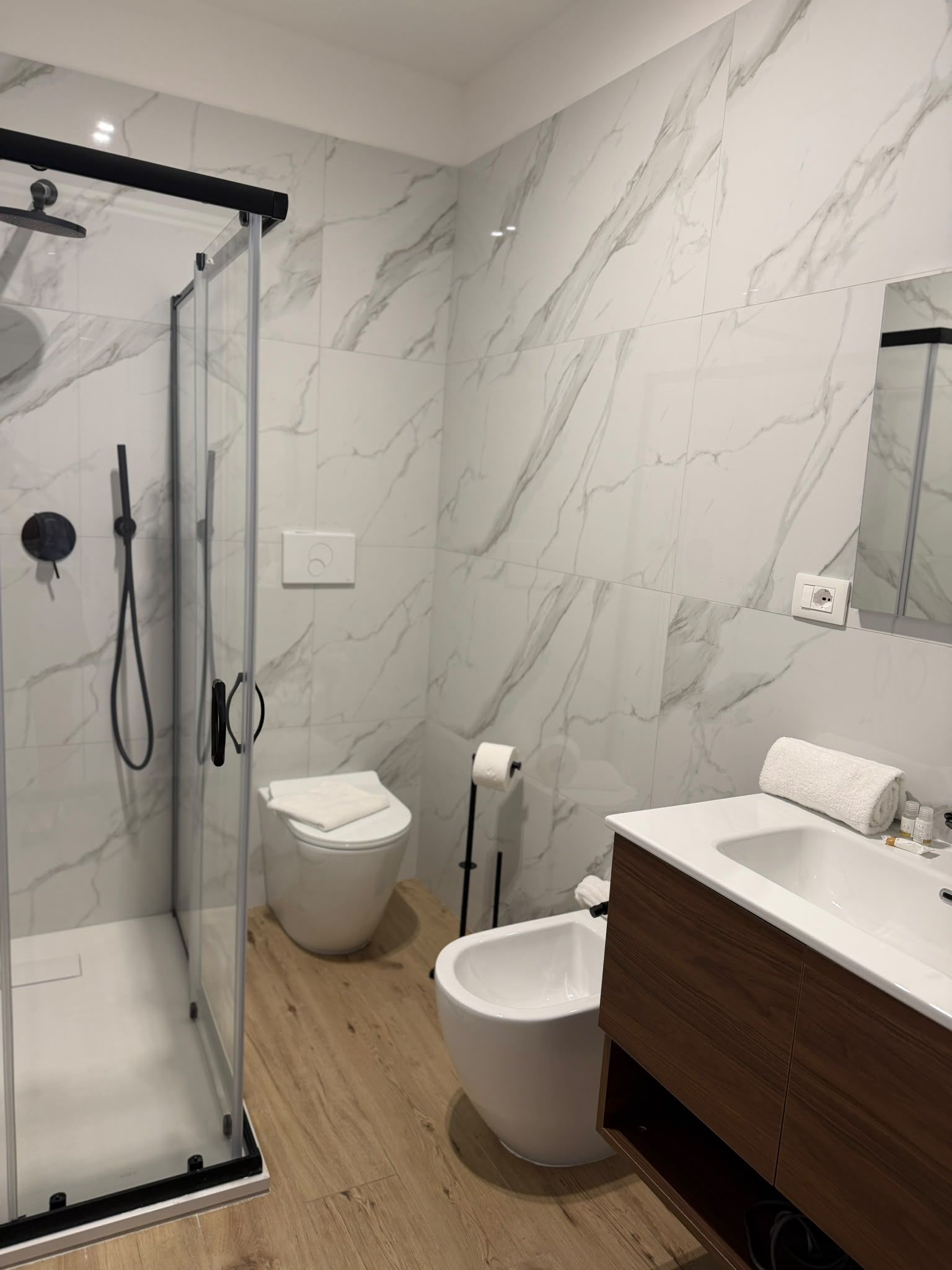 A modern bathroom with a glass-enclosed shower, a wooden vanity, and marble walls.
