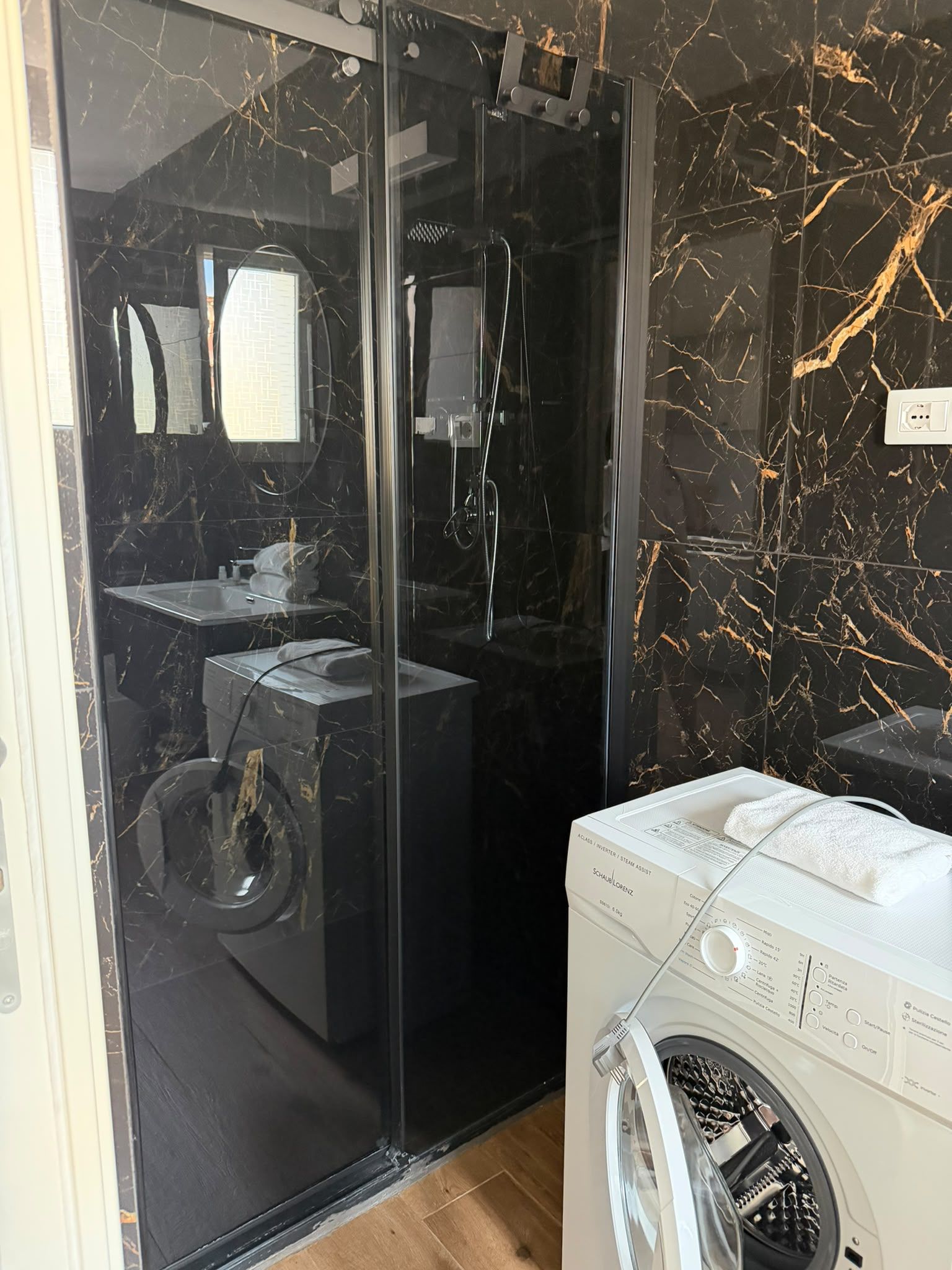 Une salle de bain moderne avec une douche à parois de verre, un lavabo intégré et un lave-linge blanc.
