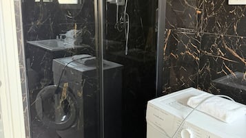 Une salle de bain moderne avec une douche à parois de verre, un lavabo intégré et un lave-linge blanc.