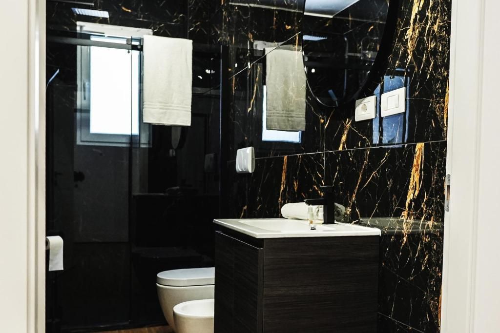 Un bagno moderno con una parete in marmo nero, un lavabo bianco e un water.