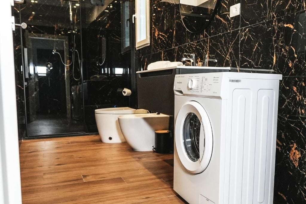 Ein modernes Badezimmer mit Waschmaschine, zwei Toiletten und einer Duschkabine aus Glas.