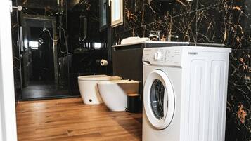 Ein modernes Badezimmer mit Waschmaschine, zwei Toiletten und einer Duschkabine aus Glas.