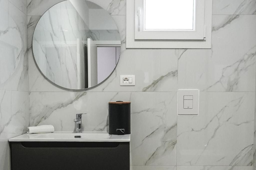 A bathroom with a marble wall, a round mirror, a sink with a faucet, a towel, and a soap dispenser.
