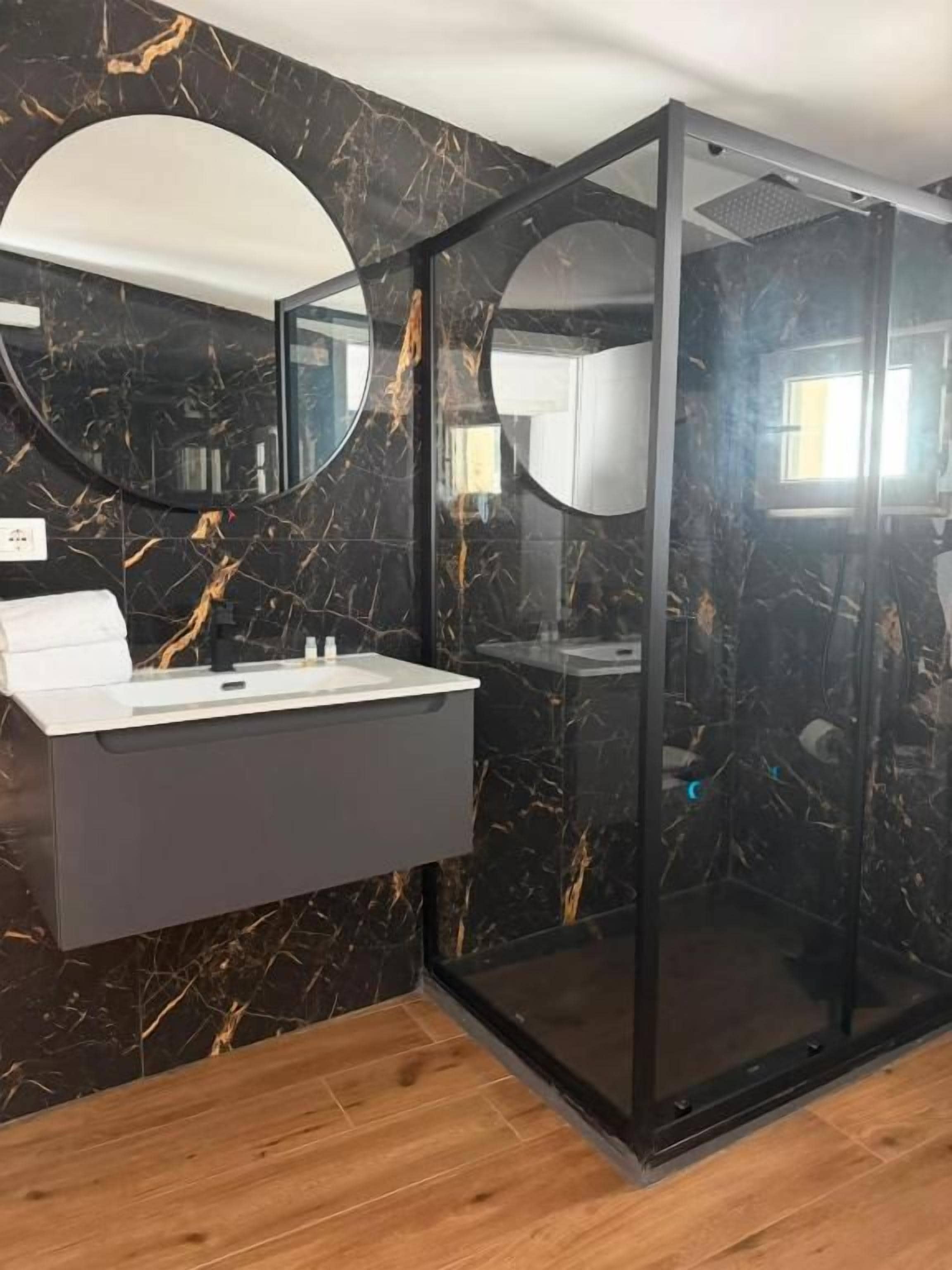 Un baño con pared de mármol, lavamanos blanco y cabina de ducha de cristal.