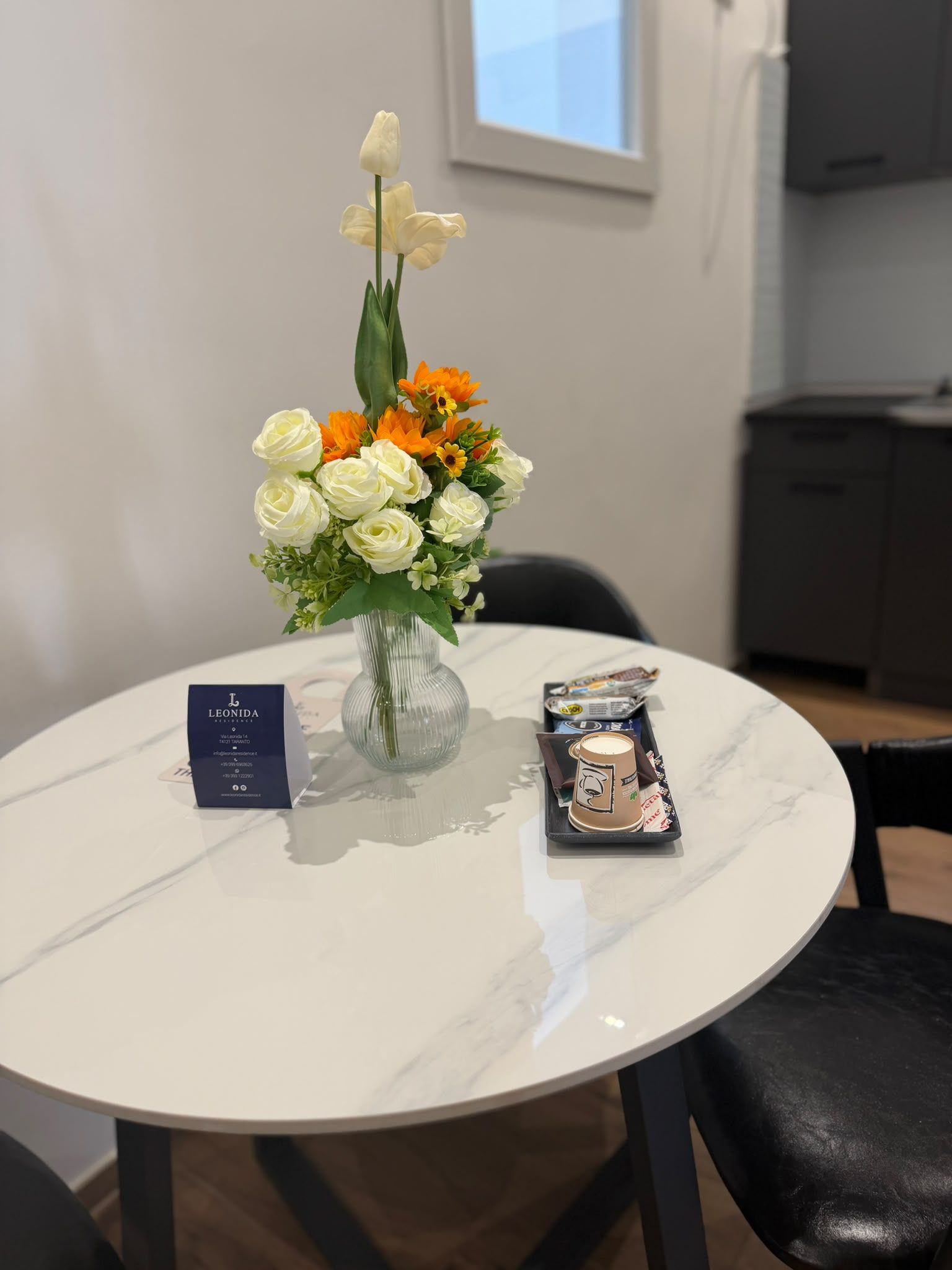 Una mesa redonda con un florero, una tarjeta de presentación y una taza de café.