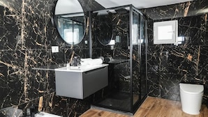 A modern bathroom with a black marble wall, a glass shower enclosure, and a wooden floor. - Leonida Residence (TARANTO)