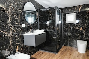 Een moderne badkamer met een wand van zwart marmer, een glazen douchecabine en een houten vloer.