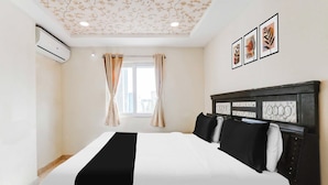 Hotellihuone, jossa on sänky, verhot, ikkuna ja seinätaideteoksia.