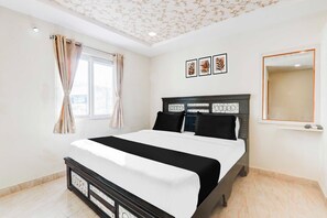 Un dormitorio con una cama, una ventana con cortinas, un espejo colgado en la pared y tres cuadros enmarcados.